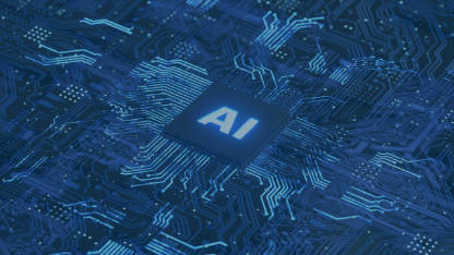 A close-up shot of a dark blue circuit board with glowing light blue lines representing circuits. In the center, there is a prominent, square microchip with the letters AI glowing brightly in light blue. The overall impression is one of advanced technology and artificial intelligence.